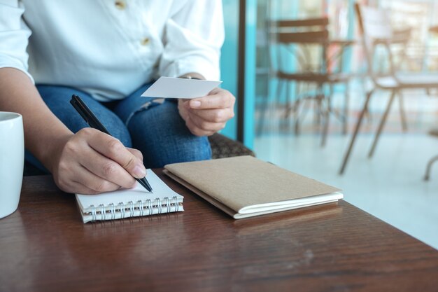 Close-upbeeld van een vrouw die een leeg leeg adreskaartje houdt tijdens het schrijven op een notitieboekje