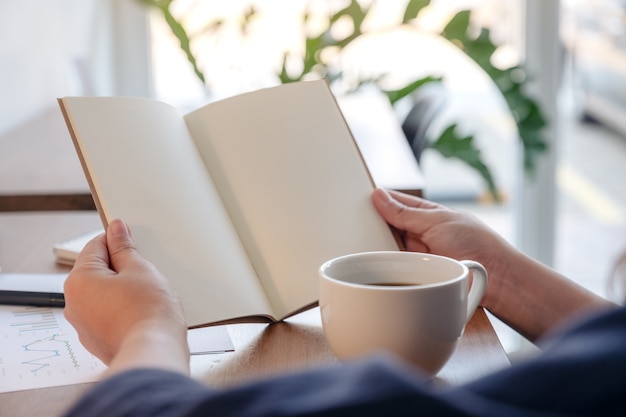 Close-upbeeld van een vrouw die een leeg notitieboekje met koffiekop en documenten op de lijst houdt en opent