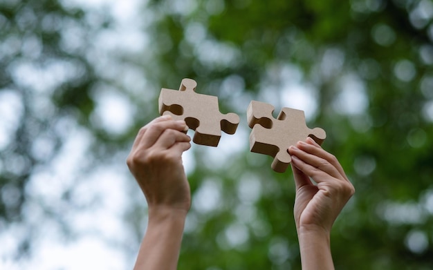 Close-upbeeld van een vrouw die een stuk houten puzzel vasthoudt en in elkaar zet in de buitenlucht