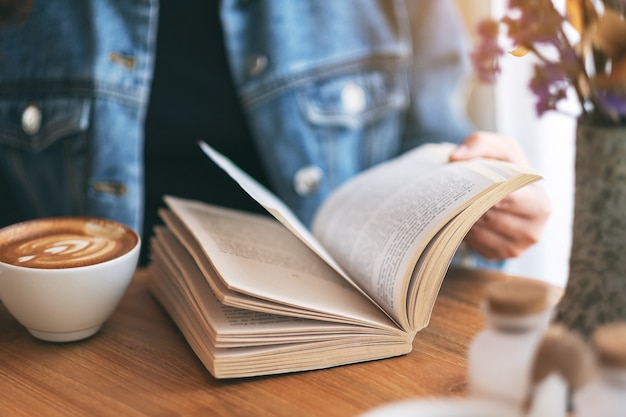 Close-upbeeld van een vrouw die een vintage romanboek vasthoudt en leest terwijl ze koffie drinkt