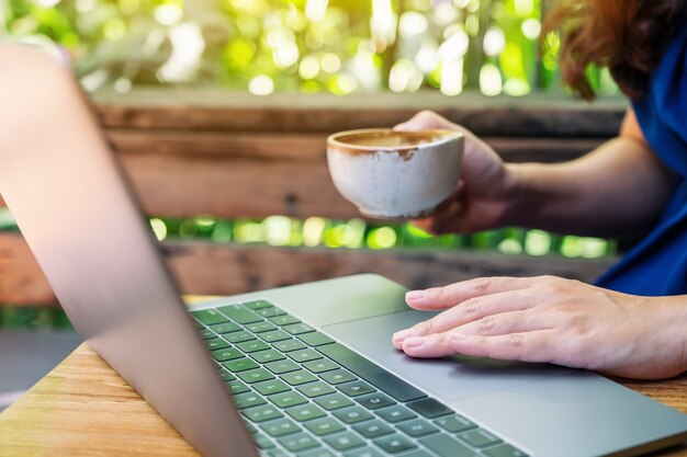 Close-upbeeld van een vrouw die het touchpad van een laptop gebruikt en aanraakt terwijl ze koffie drinkt