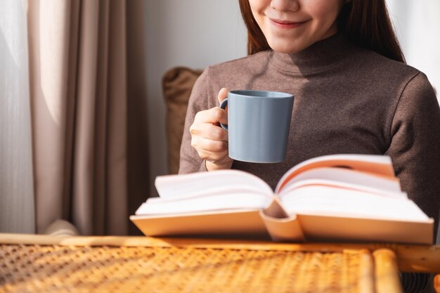 Close-upbeeld van een vrouw die koffie drinkt terwijl ze thuis een boek leest