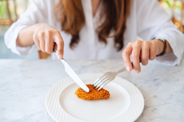 Close-upbeeld van een vrouw die mes en vork gebruikt om gebraden kip in restaurant te eten