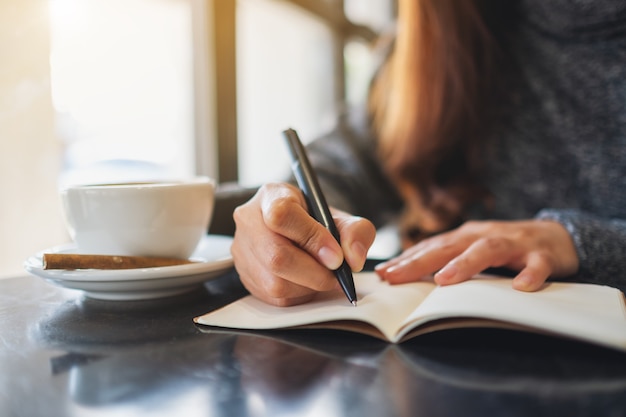 Foto close-upbeeld van een vrouw die op een leeg notitieboekje op de tafel schrijft