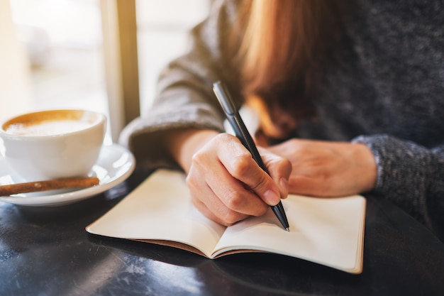 Close-upbeeld van een vrouw die op een leeg notitieboekje op de tafel schrijft