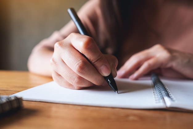 Close-upbeeld van een vrouw die op een leeg notitieboekje op houten tafel schrijft