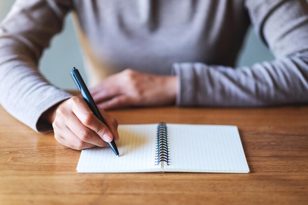 Close-upbeeld van een vrouw die op een leeg notitieboekje op tafel schrijft