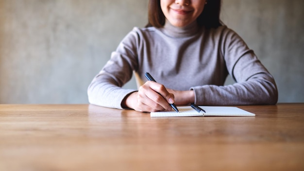Close-upbeeld van een vrouw die op een leeg notitieboekje op tafel schrijft