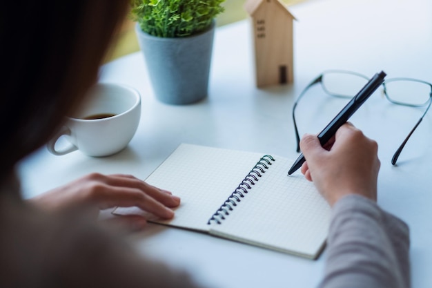 Close-upbeeld van een vrouw die op een leeg notitieboekje op tafel schrijft