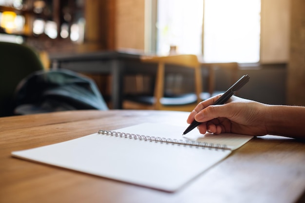 Close-upbeeld van een vrouw die op een leeg notitieboekje op tafel schrijft