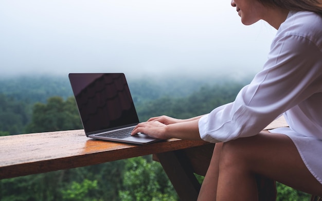 Close-upbeeld van een vrouw die op een mistige dag een laptop gebruikt en eraan werkt terwijl ze op een balkon zit met een prachtig uitzicht op de natuur