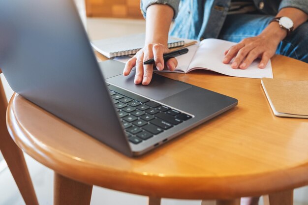 Close-upbeeld van een vrouw die op een notitieboekje schrijft terwijl ze op een laptop op kantoor werkt