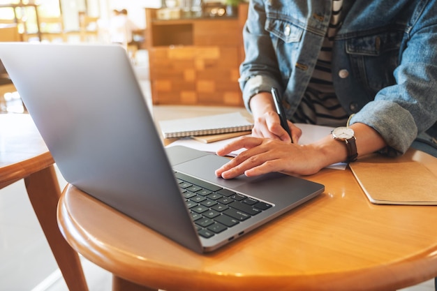 Close-upbeeld van een vrouw die op een notitieboekje schrijft terwijl ze op een laptop op kantoor werkt