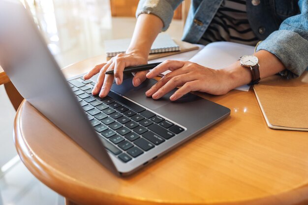 Close-upbeeld van een vrouw die op een notitieboekje schrijft terwijl ze op een laptop op kantoor werkt