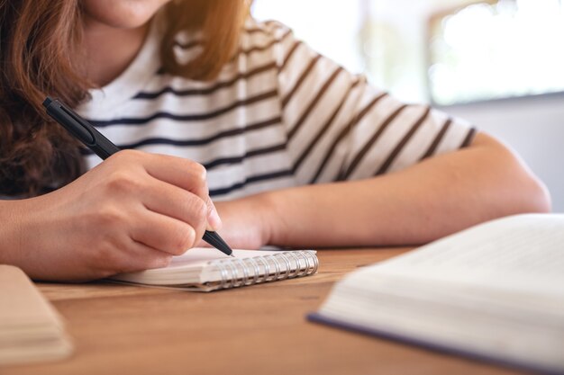 Close-upbeeld van een vrouw die op lege notitieboekje met boeken op houten lijst schrijft tijdens het leren