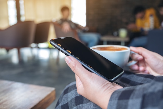 Close-upbeeld van een vrouw die slimme telefoon houdt, gebruikt en bekijkt terwijl het drinken van koffie in koffie