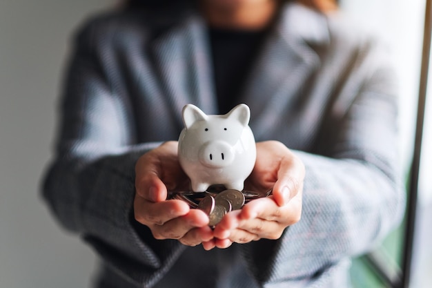 Close-upbeeld van een vrouw die spaarvarken en muntstukken in handen houdt om geld en financieel concept te besparen