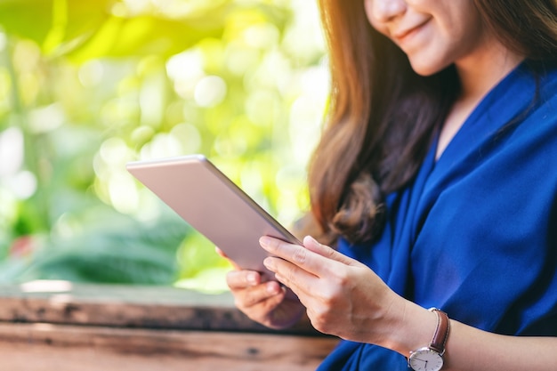 Close-upbeeld van een vrouw die tablet-pc vasthoudt en gebruikt terwijl ze in de tuin zit