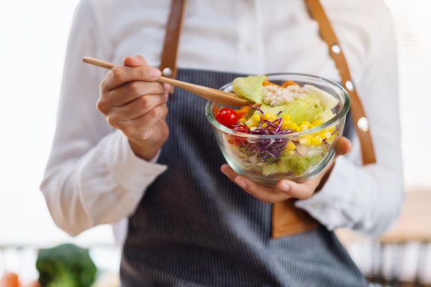 Close-upbeeld van een vrouw die verse gemengde groentensalade in keuken kookt en eet