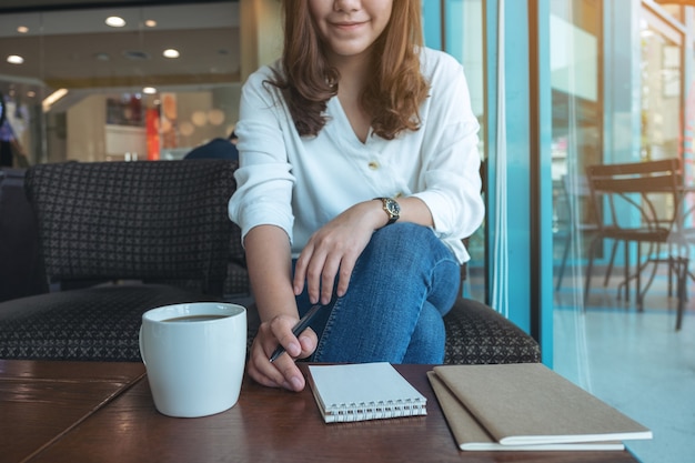 Close-upbeeld van een vrouw die voorbereidingen treft om op leeg notitieboekje met koffiekop op houten lijst te schrijven