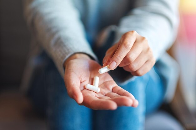 Close-upbeeld van een vrouw die witte medicijncapsules in de hand houdt en plukt