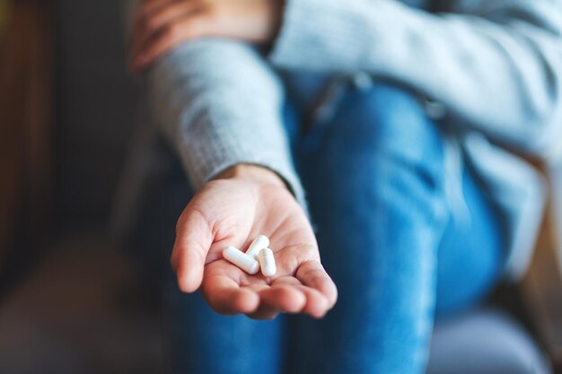 Close-upbeeld van een vrouw die witte medicijncapsules in de hand houdt