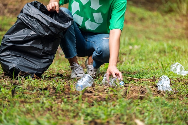 Close-upbeeld van een vrouwelijke activist die plastic afvalflessen oppakt in een plastic zak in het park voor recyclingconcept