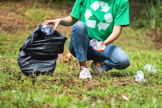 Close-upbeeld van een vrouwelijke activist die plastic afvalflessen oppakt in een plastic zak in het park voor recyclingconcept