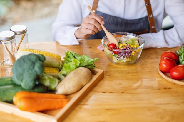 Close-upbeeld van een vrouwelijke chef-kok die een kom verse gemengde groentensalade in keuken kookt en eet