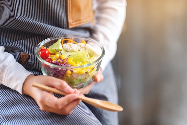 Close-upbeeld van een vrouwelijke chef-kok die een kom verse gemengde groentensalade kookt en vasthoudt om in de keuken te eten