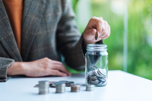 Close-upbeeld van een zakenvrouw die munten verzamelt en in een glazen pot doet