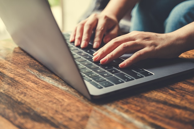 Close-upbeeld van handen die en op laptop toetsenbord op houten lijst gebruiken typen