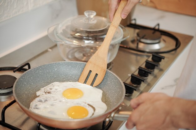 Close-upbeeld van man die eieren op keukenfornuis frituurt
