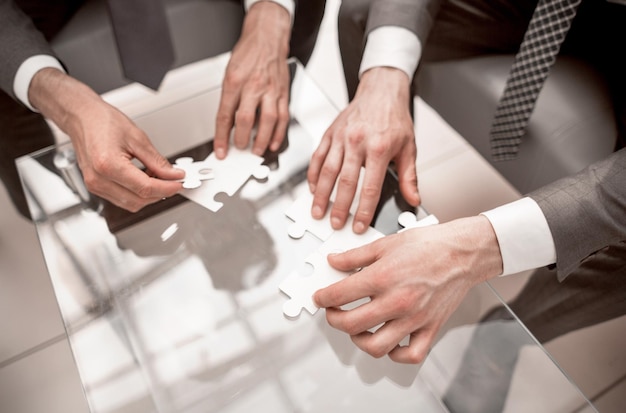 Close upbusiness people putting together a puzzle sitting behind a Desk