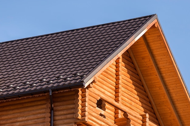 Close-updetail van nieuwe moderne houten warme ecologische cottagehuisbovenkant met shingled bruin dak en houten zijspanten op blauwe hemel Professioneel gedaan timmerwerk en bouwwerkzaamheden.