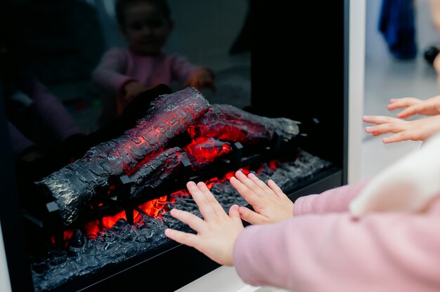 Close-upfoto van de handen die van kinderen door een open haard verwarmen. Voel je thuis comfortabel rond het kampvuur.