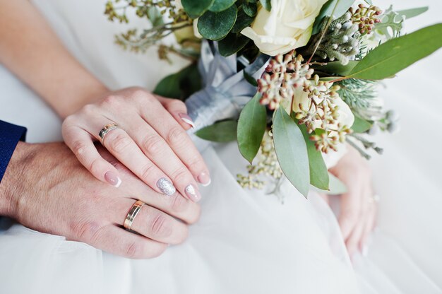 Close-upfoto van de handen van de bruidegom en van de bruid met ringen en boeket.