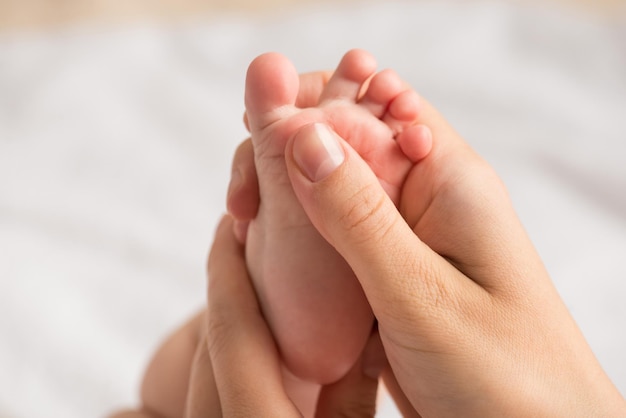 Close-upfoto van de handen van de moeder die de uiterst kleine voet van de baby masseren op geïsoleerde witte achtergrond