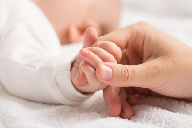 Close-upfoto van de kleine hand van de pasgeborene die de wijsvinger van de moeder op geïsoleerde witte textielachtergrond klemt