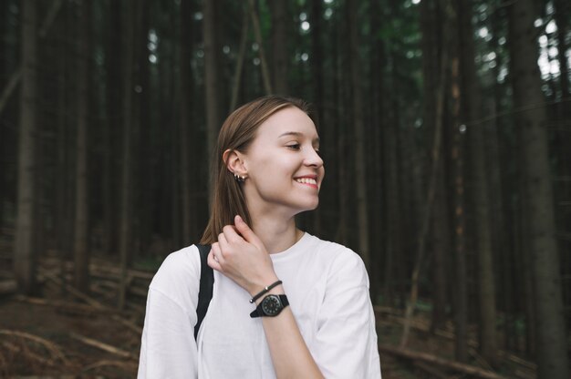 Close-upfoto van een glimlachende jonge wandelaarvrouw in het sparrenbos die positief en gelukkig voelt