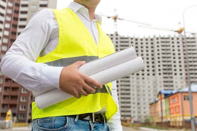 Close-upfoto van een ingenieur die opgerolde blauwdrukken vasthoudt op de bouwplaats