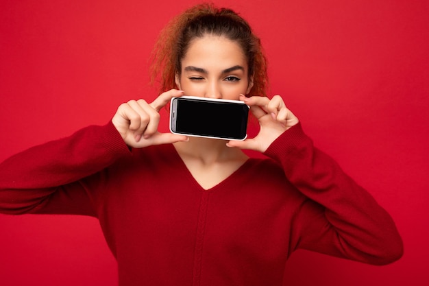 Close-upfoto van gelukkige grappige jonge vrouwelijke persoon die donkerrode sweater draagt