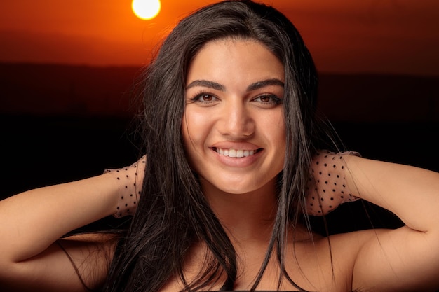 Close-upfoto van het hete model bij zonsondergang die lacht en haar handen tegen haar nek houdt Foto van hoge kwaliteit