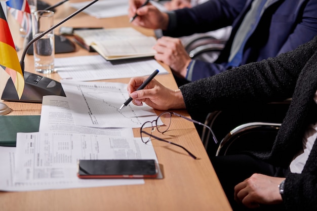 Close-upfoto van mensen die aan bureau zitten dat notities, met documenten, persconferentie maakt. zakelijke of politieke bijeenkomst in de directiekamer