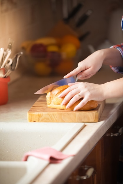 Close-upfoto van vrouw die brood op houten bureau snijdt