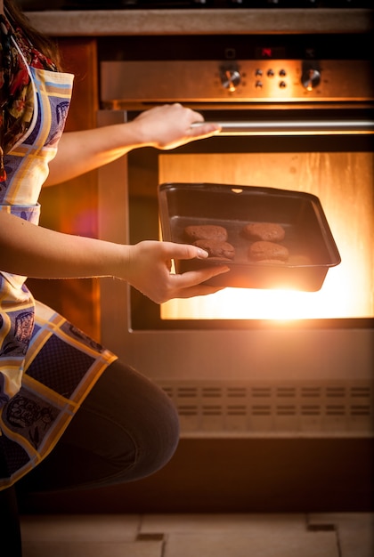 Close-upfoto van vrouw die chocoladekoekjes in oven kookt