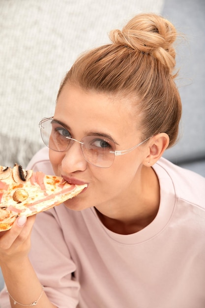 Close-upgezicht van blonde vrouw die in glazen stuk pizza eet