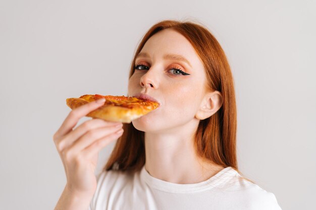 Close-upgezicht van gelukkige aantrekkelijke jonge vrouw met eetlust die heerlijke pizza eet die camera bekijkt