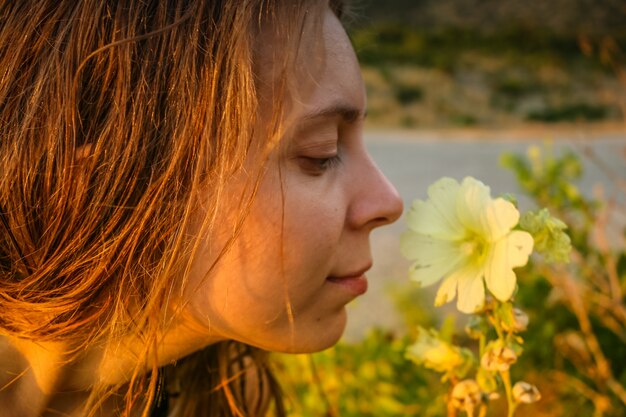 Foto close-upgezicht van jong meisje en gele bloem bij de zomerzonsondergang.