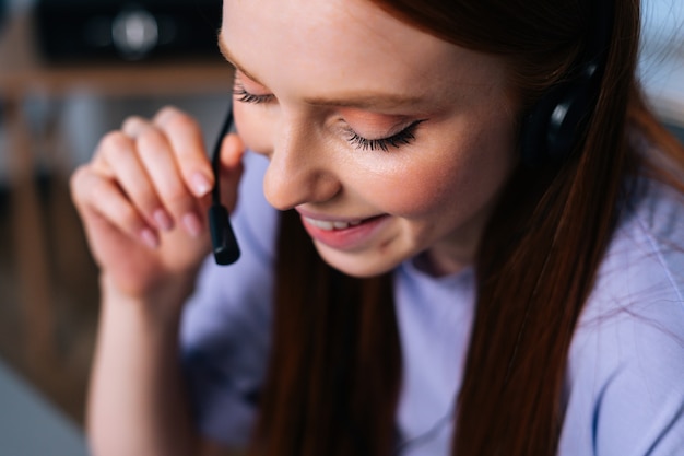 Close-upgezicht van vrolijke jonge vrouwenexploitant die hoofdtelefoon gebruikt tijdens klantenondersteuning op kantoor